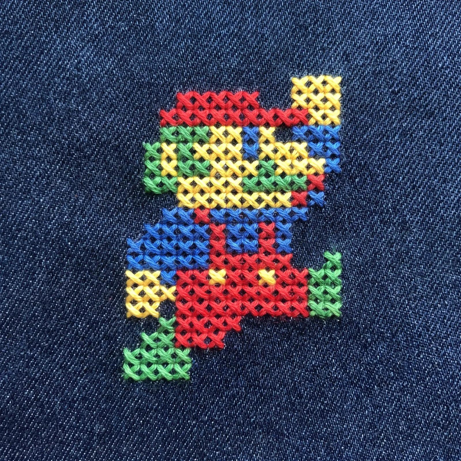 Cross Stitch On Denim, A pixel style motif stitched in bright thread across woven denim
