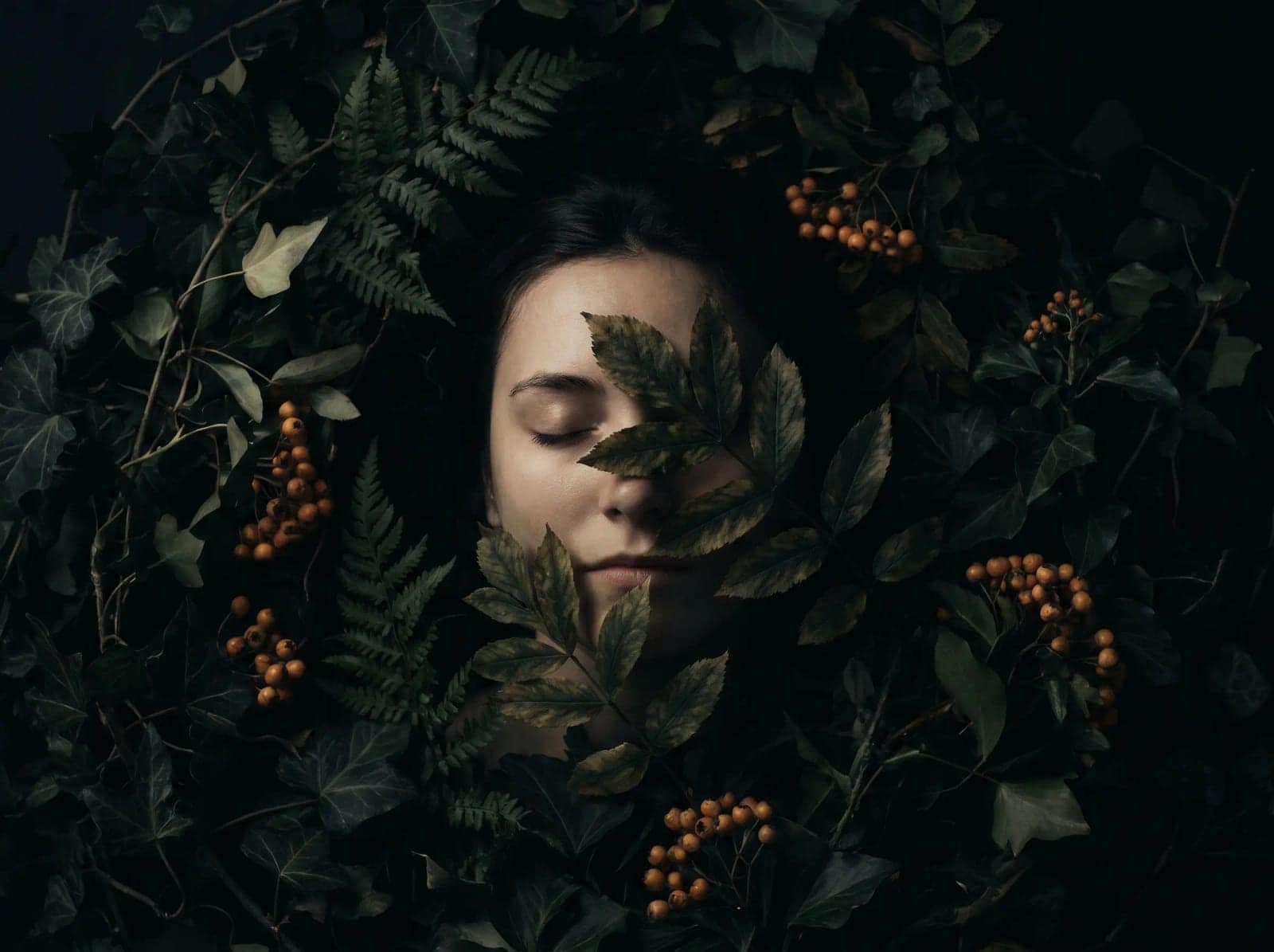 Dark Botanical Portrait, A face half buried in leaves, lit like a Dutch still life